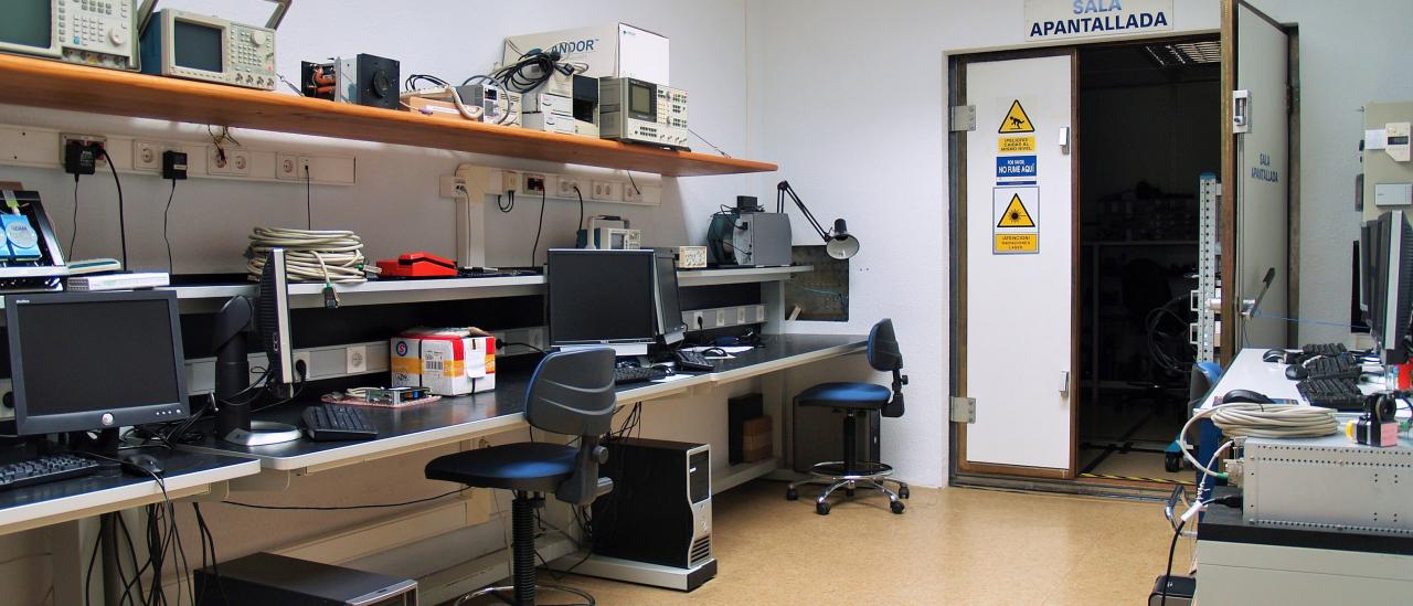 General view of the Electromagnetic Compatibility Laboratory with workbenches and computers and view in the background of the entrance to the shielded room