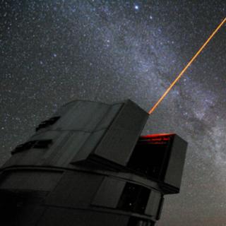 A laser beam launched from the VLT's Yepun telescope and in background a majestic view of the southern sky, with the disc of the Milky Way crossing the image and the Magellanic Clouds on the top right A view of our Milky Way galaxy with its close neighbors the Magellanic Clouds