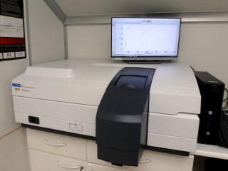 View of the spectrophotometer in the laboratory. Medium sized device placed on a table with a trap door to place the samples to be measured and a computer and monitor for its control